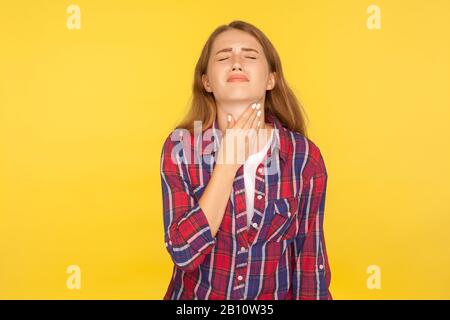 Portrait de la jeune femme malade en chemise à damier touchant le cou douloureux, grimaçant de la douleur, des amygdales de douleur, ayant des troubles thyroïdiens et des symptômes de grippe. In Banque D'Images