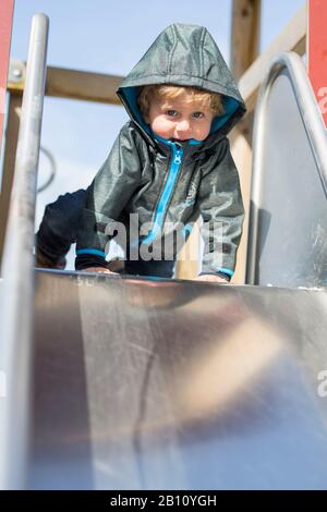 Petit garçon avec une capuche sur un toboggan Banque D'Images