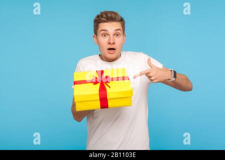 WOW, regardez mon cadeau! Enchanté homme étonné dans un t-shirt pointant vers la boîte enveloppée et regardant la caméra avec étonnement, surpris par le présent, inattendu Banque D'Images