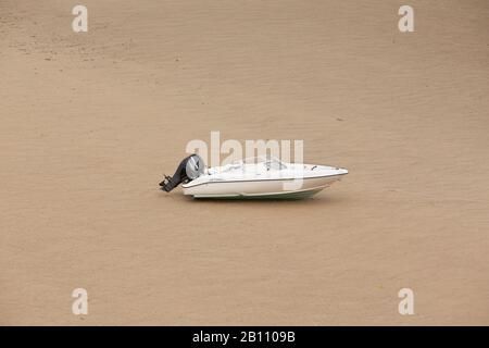 Hors-bord en fibre de verre blanche avec moteur hors-bord noir sur une plage de sable sec à marée basse à abersoch sur la côte nord du pays de galles au royaume-uni Banque D'Images