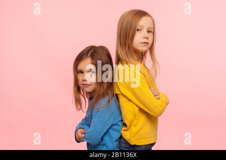 Amitié, solidarité et soutien. Deux filles d'âge préscolaire merveilleuses se tenant de dos à dos, regardant l'appareil photo avec confiance attentif sérieux expressi Banque D'Images