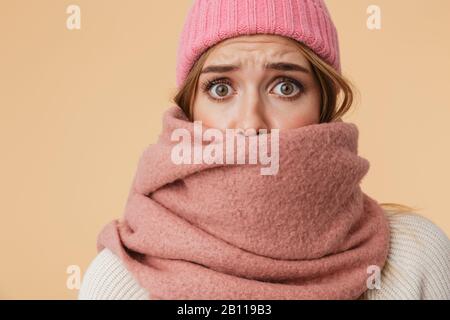 Image de la jeune fille caucasienne portant un chapeau d'hiver et un foulard frognant et étant surpris isolé sur fond beige Banque D'Images