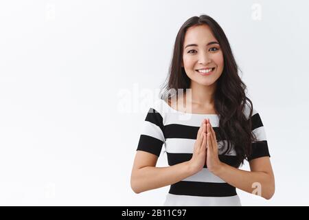 Tendre, gai et sympathique-regardant paisible jeune femme asiatique tenir les mains en priant et souriant reconnaissant, exprimer sa gratitude pour l'aide Banque D'Images