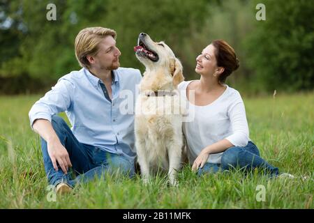 Couple assis sur la prairie avec labrador Banque D'Images