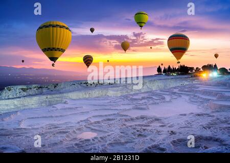 Ballons en air chaud et piscines naturelles en travertin au coucher du soleil à Pamukkale, en Turquie. Banque D'Images