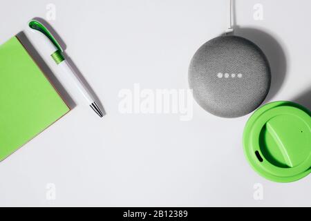 Concept d'assistant numérique. Enceinte plate avec éclairage LED activée avec bloc-notes vert court, stylo et tasse à café réutilisable. Banque D'Images