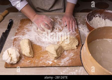 Une femme pétrit la pâte. Planche à découper en contreplaqué, grille à farine en bois et broche à roulettes en bois - outils pour la fabrication de la pâte. Banque D'Images