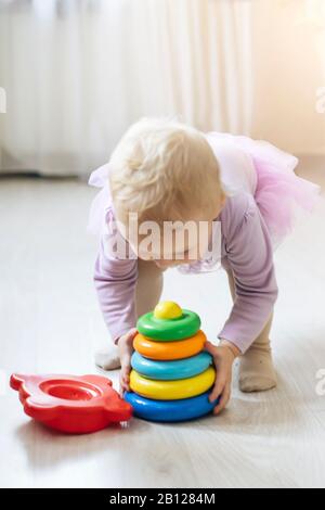 fille porte la pyramide jouet. enfant dans la salle de séjour baigné de soleil. Jouets éducatifs pour enfants de moins de 2 ans. Jouet multicolore bleu, jaune, rouge, gre Banque D'Images