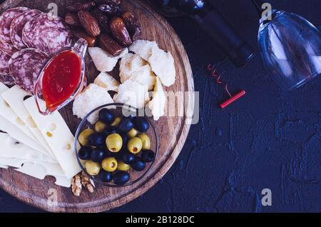 Bouteille de vin avec verre à vin, tire-bouchon et antipastis sur fond sombre. Planche en bois pleine de hors-d'œuvre méditerranéens, tapas ou antipasto. Assortiment Banque D'Images