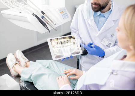 Dentiste professionnel montrant les dents de la radiographie dans le pavé tactile à son patient Banque D'Images