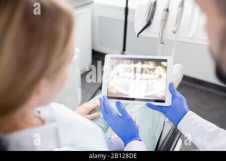 Les mains gantées du dentiste avec un comprimé montrant la radiographie des dents du patient féminin Banque D'Images