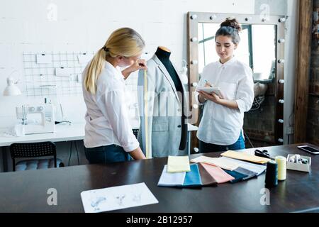 L'un des deux jeunes créateurs de mode mesurant la longueur de la gaine de veste Banque D'Images