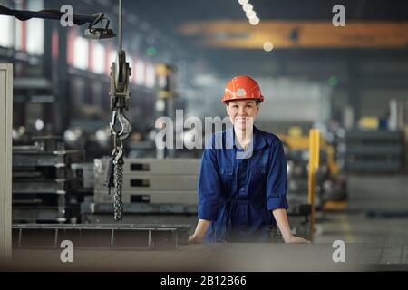 Jeune femme gaie en tenue de travail et casque de protection vous regardant Banque D'Images