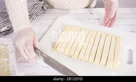 Étape par étape. Coupe de fudge de canne à sucre fait maison sur un tableau de découpe blanc. Banque D'Images