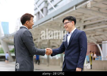les gens d'affaires se tenant à la main sur l'accord d'affaires ou le travail d'équipe contre le bâtiment Banque D'Images