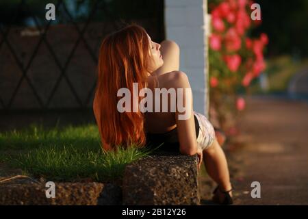 Jeune femme couchée sur un mur de brique dans la lumière du soleil Banque D'Images