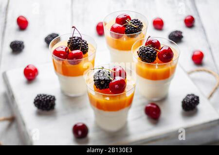 4 tasses de manguier pannacota sur un plateau en bois avec des mûres et des cerises Banque D'Images