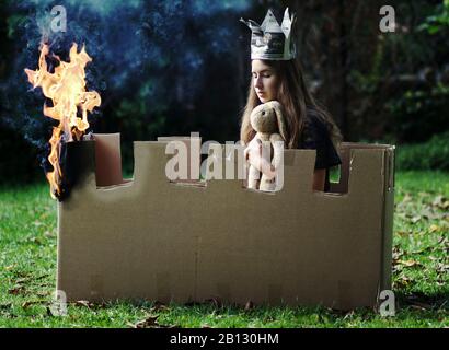 Jeune fille avec jouet en peluche et papier se trouve dans un château en feu fait ?? de carton Banque D'Images