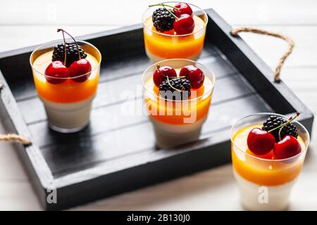 4 tasses de manguier pannacota sur un plateau en bois avec des mûres et des cerises Banque D'Images