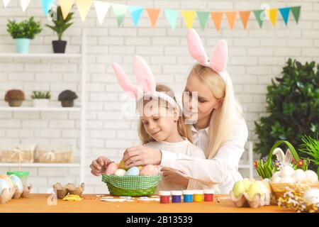 Joyeuses pâques. La fille et la mère aux oreilles de lapin décorent les œufs de Pâques assis à une table Banque D'Images