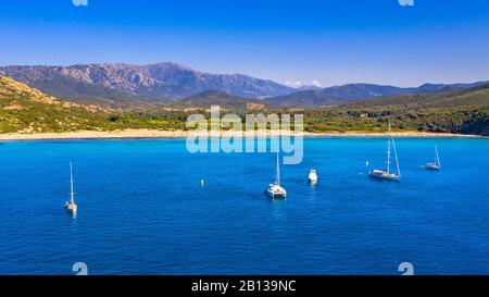 Voiliers amarré dans la baie naturelle avec plage sur la côte accidentée de la Corse, France Banque D'Images