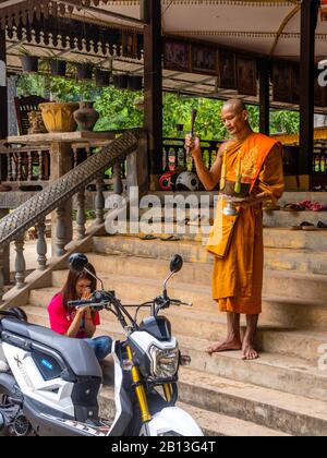 Une jeune femme reçoit une bénédiction pour son scooter motorisé d'un jeune moine dans un temple bouddhiste. Parc Archéologique D'Angkor Wat, Siem Reap, Cambodge. Banque D'Images