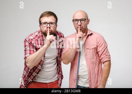 Deux hommes disent le silence, faisant un geste avec un index sur leurs lèvres et regarder excitement à la caméra. Secret des amis. Shh. Banque D'Images