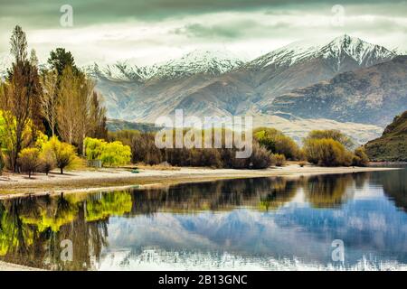 Les alpes du sud enneigées se reflètent dans l'eau sans motionelle du lac bordée d'arbres colorés Banque D'Images