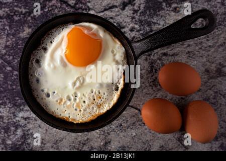 Côté ensoleillé, oeuf frit dans une poêle en fonte avec œufs entiers sur fond de béton. Vue de dessus Banque D'Images