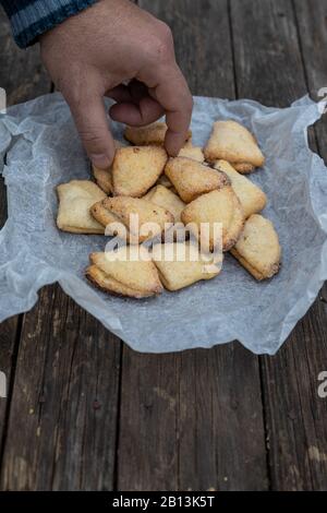 La main de l'homme prend la caillebotte biscuit avec triangles sur parchemin blanc sur un vieux fond de bois foncé Banque D'Images