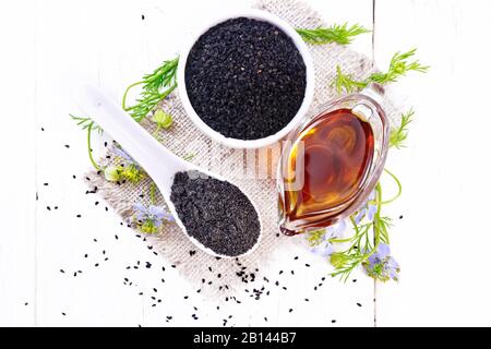 Farine Nigella sativa dans une cuillère, graines de cumin noires dans un bol et huile dans un bateau à sauce sur le burap, branches de kalingi avec des fleurs bleues et des feuilles vertes sur Banque D'Images