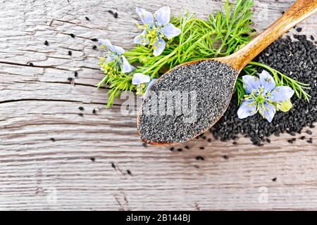 Farine de Nigella sativa dans la cuillère avec une fleur et des feuilles de kalingini sur un fond d'un vieux panneau en bois d'en haut Banque D'Images