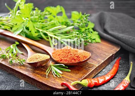 Poivre rouge chaud moulu et paprika dans des cuillères, des gousses de piment, des légumes épicés et une serviette sur fond de planche en bois Banque D'Images