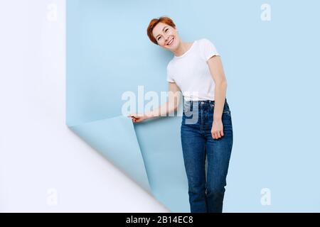 Jolie jolie jolie femme avec des cheveux courts au gingembre qui tirent un bout de revêtement d'un mur Banque D'Images