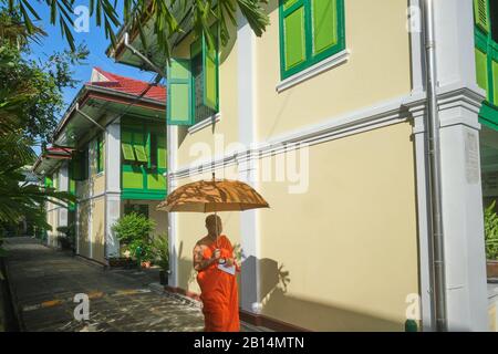 Un moine avec un parapluie marchant devant les logements des moines dans le parc de Wat Benchamabohit (temple de marbre) à Bangkok, Thaïlande Banque D'Images