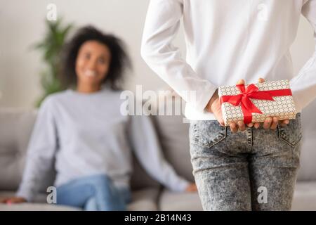 Vue arrière de la fille africaine adolescente qui tient un cadeau derrière le dos Banque D'Images