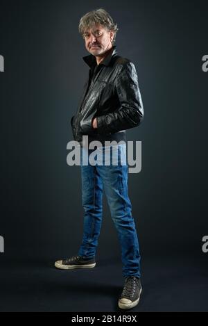 Portrait d'un homme avec veste en cuir et pantalon denim sur fond dégradé Banque D'Images