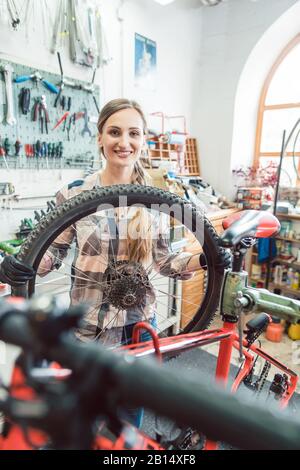 Mécanicien vélo femme regardant à travers la roue de bicyclette Banque D'Images