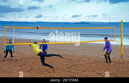 Portobello Beach, Édimbourg, Écosse, Royaume-Uni. 23 février 2020. Départ raisonnablement calme, soleil et température de 3 degrés. Lever de soleil nuageux se brisant au soleil éclatant tôt le matin, exercice énergique avec volley-ball sur la plage, avec l'île d'Inchkieth sur le Firth of Forth en arrière-plan. Banque D'Images