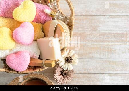 Accessoires de bain relaxants avec bombes de bain en forme de coeur jaune et rose, brosse de corps, sérum, palo santo, serviettes et fleur sur un fond en bois. Relaxation, spa, cosmétiques de beauté pour le concept de traitement du corps. Banque D'Images