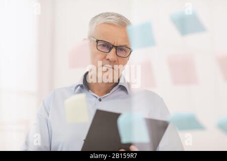 Manager mûr pensif regardant des notes collantes sur le verre Banque D'Images