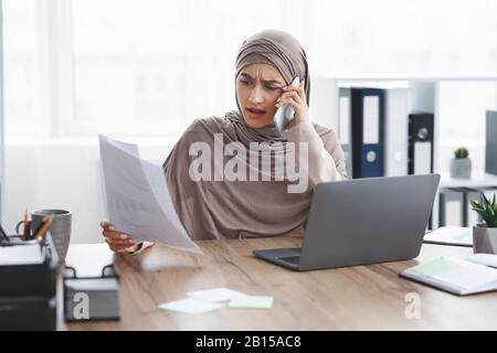 A souligné la femme d'affaires musulmane qui vérifie la documentation et parle sur le téléphone portable au bureau Banque D'Images