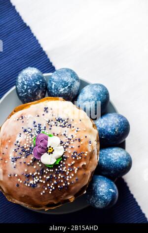 Gâteau de Pâques décoré de fleur de sucre et d'œufs de couleur bleue sur une plaque sur fond de tissu blanc et bleu avec espace de copie. Les œufs étaient de couleur bleu wi Banque D'Images
