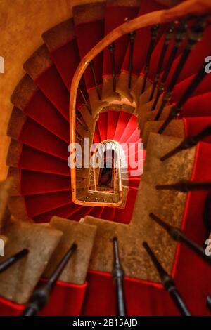 Vue vertigineuse sur l'escalier en colimaçon asymétrique à moquette rouge avec balustrade en chêne d'un hôtel de palais médiéval de Prague Banque D'Images