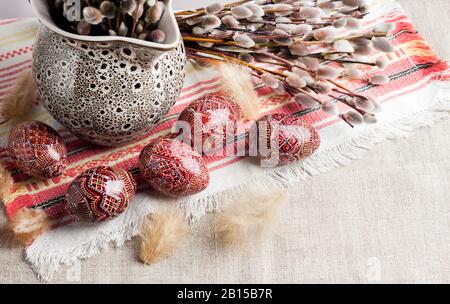 Pâques toujours la vie avec Pysanka et branches de saule dans la carafe en céramique sur le tissu ukrainien traditionnel. Œufs de Pâques décorés, traditionnels pour l'Europe de l'est Banque D'Images