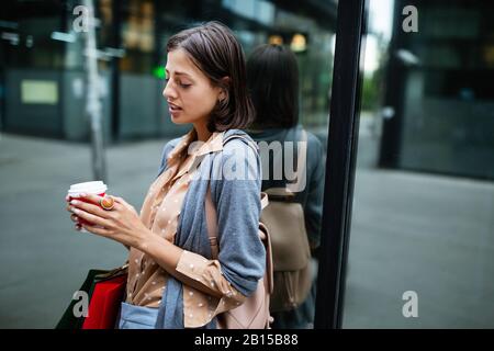 Une jeune femme heureuse à boire du café et à marcher avec des sacs après avoir fait du shopping en ville. Banque D'Images