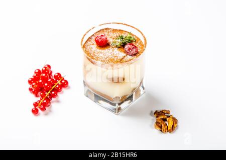 Dessert Panna cotta dans un verre transparent. Le dessert est décoré de sucre en poudre et de baies de canneberges. Un verre sur un fond blanc, à côté d'un wal Banque D'Images