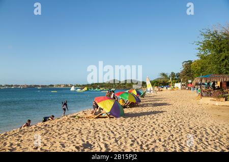 Plage de sable une journée ensoleillée avec des gens qui s'amusent sur la plage au soleil et se baignent en mer et se prometent sous les parasols Banque D'Images