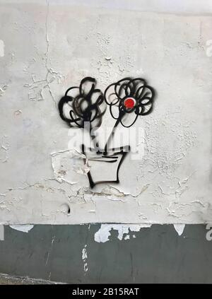 Deux fleurs noires avec cercle rouge au centre peint sur le mur fissuré blanc avec bordure grise, graffitis. Banque D'Images
