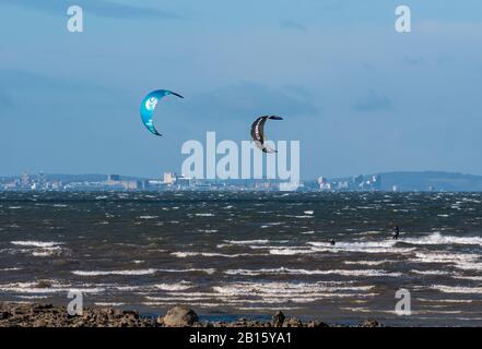 Firth Of Forth, East Lothian, Écosse, Royaume-Uni, 23 Février 2020. Météo britannique : vent très fort sur la côte avec soleil. Le vent crée des calottes blanches dans la mer et de grandes vagues contre le rivage. Les surfeurs du cerf-volant font le maximum des conditions venteuses à Longniddry Bents avec le contour d'Édimbourg au loin Banque D'Images